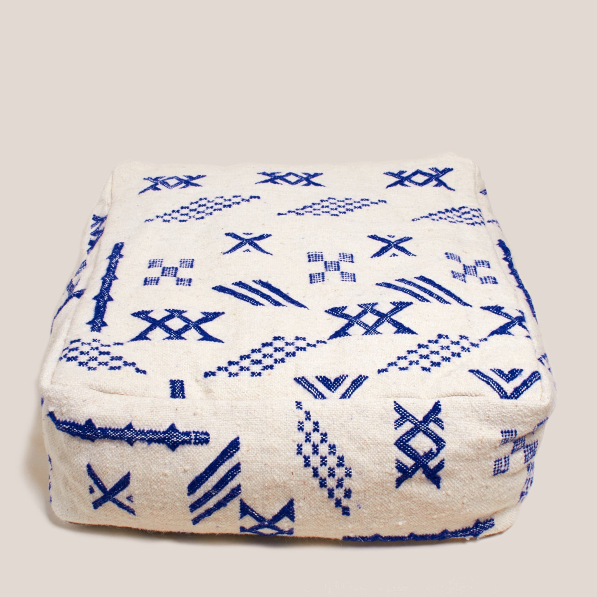 Beige Moroccan wool pouf with blue Berber geometric patterns, 60×60×20 cm, handcrafted artisan floor cushion